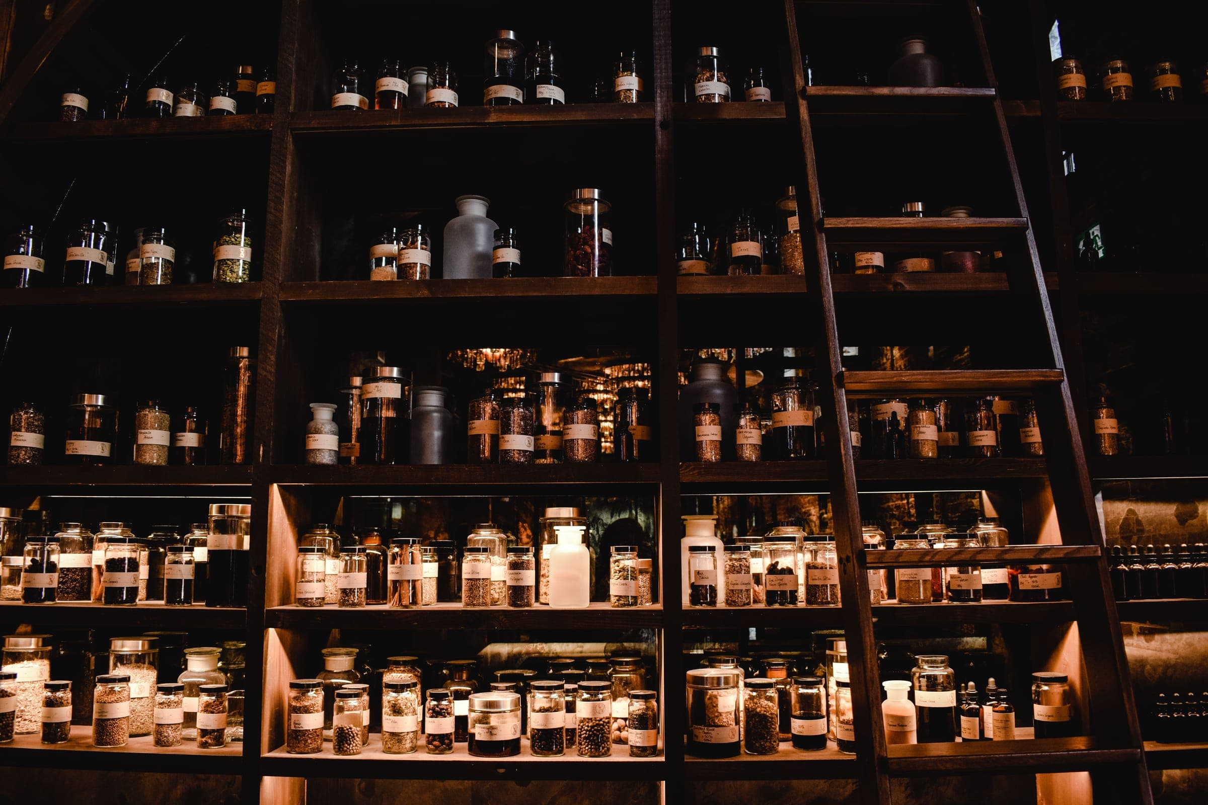 Dark wooden pharmacy shelving filled with jars, with a library ladder