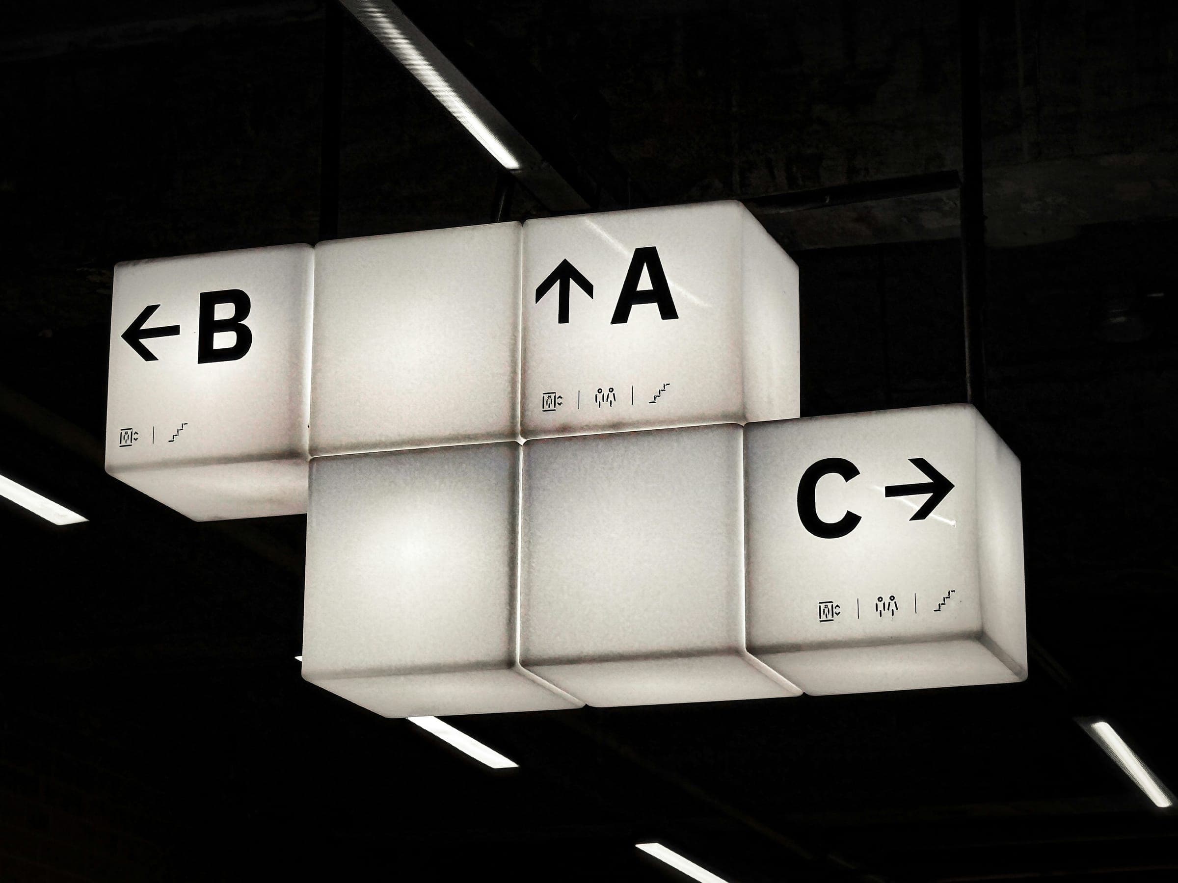 Illuminated hanging wayfinding signs pointing to areas A, B and C